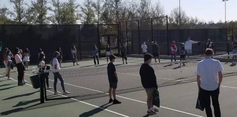 Tennis team players gather around the tennis courts during practice. 